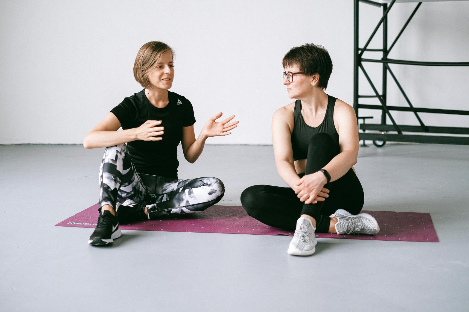 Personal trainer and client sitting together on yoga mat on floor discussing exercise plan