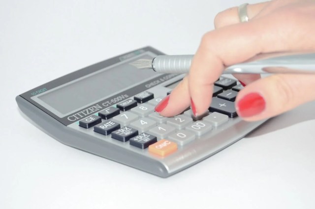 Woman's hand using a calculator to figure out the cost of hiring employees Woman's hand using a calculator to figure out the cost of hiring employees