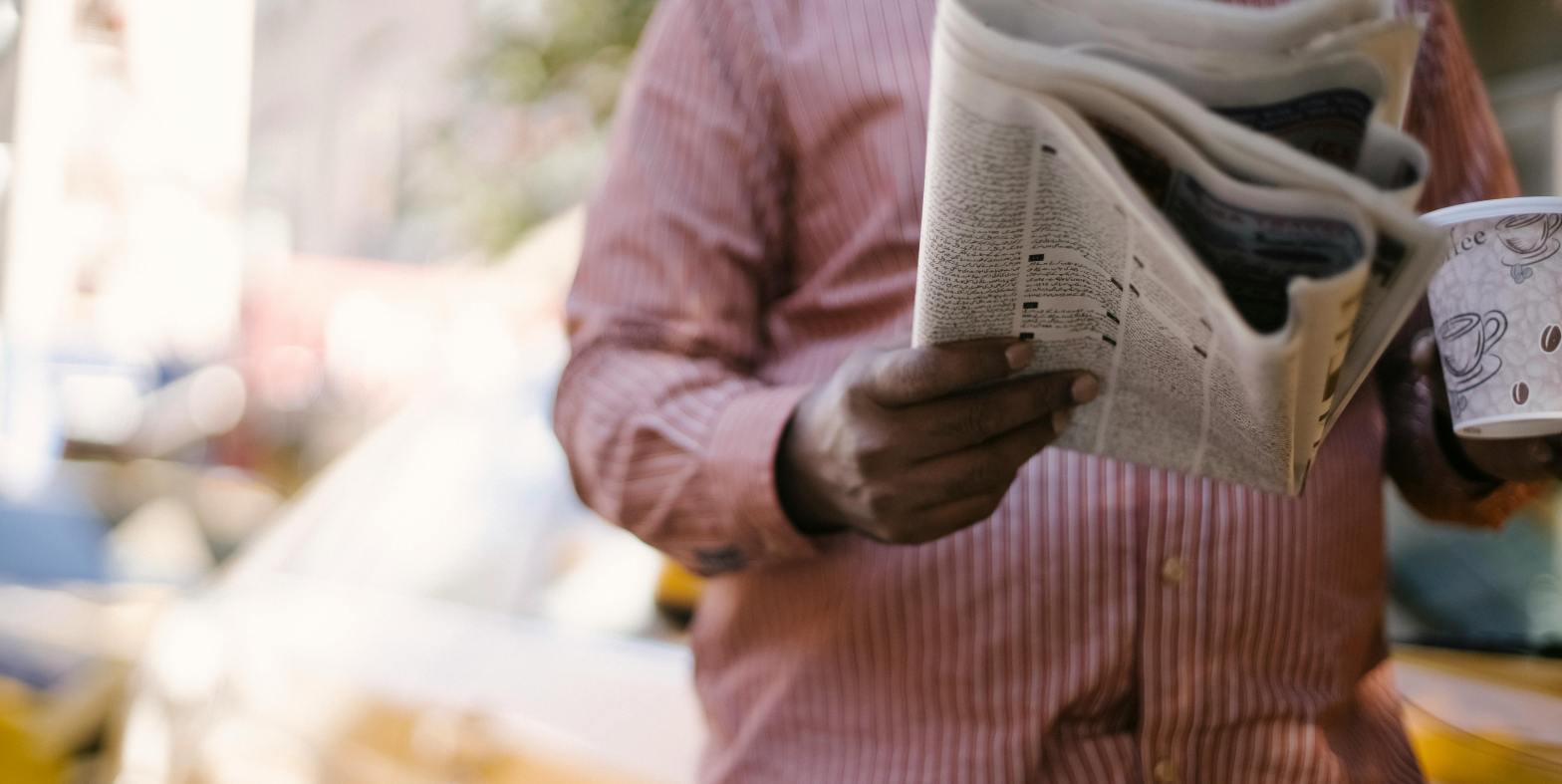 Person reading newspaper while drinking coffee