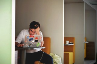 Man sitting at a table in front of a laptop computer with hands in hair to depict the frustration when you buy an article that's poorly written Man sitting at a table in front of a laptop computer with hands in hair to depict the frustration when you buy an article that's poorly written