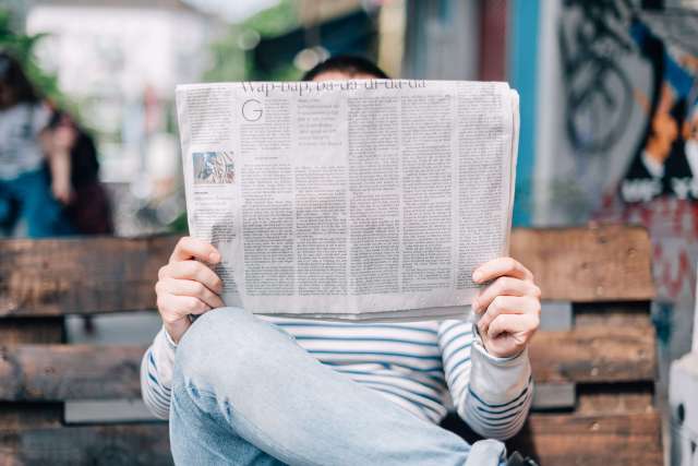 Person reading a newspaper on a park bench