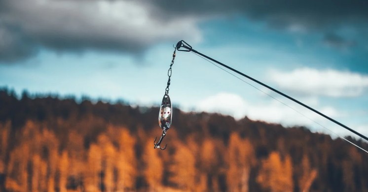 image of a fishing lure dangling above the water image of a fishing lure dangling above the water