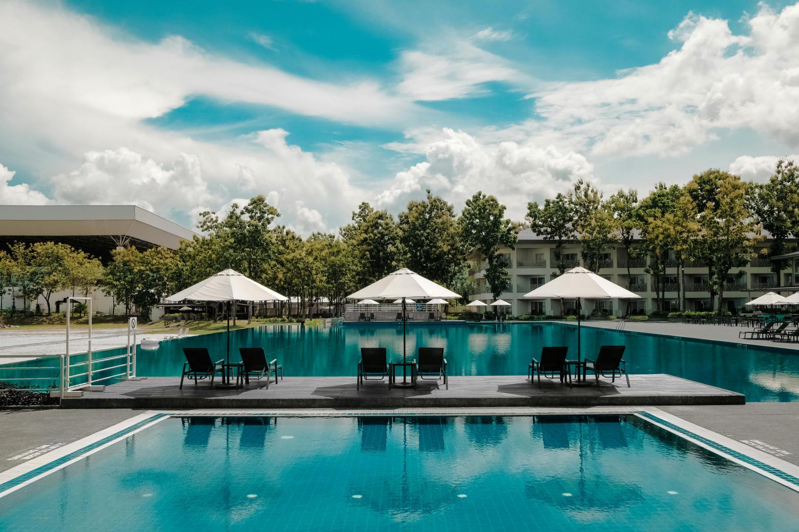 Resort with two pools surrounded by concrete patio with tables and chairs on gorgeous summer day